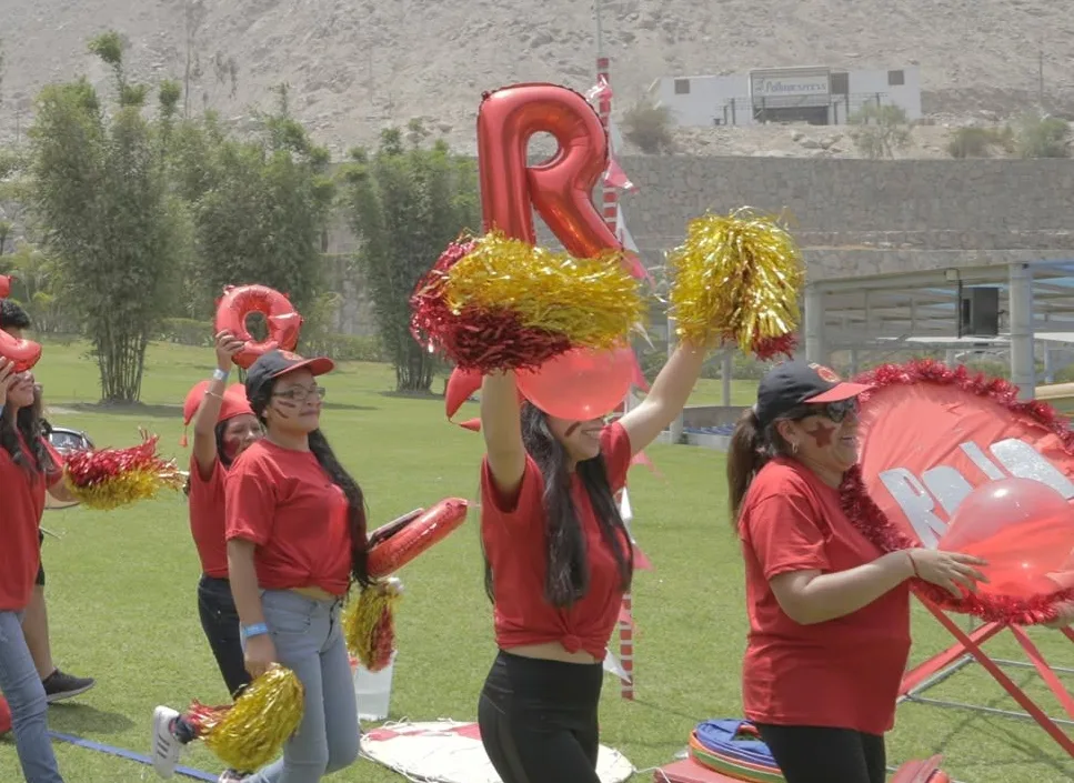 Un equipo con polos rojos anima con pompones durante una competencia al aire libre